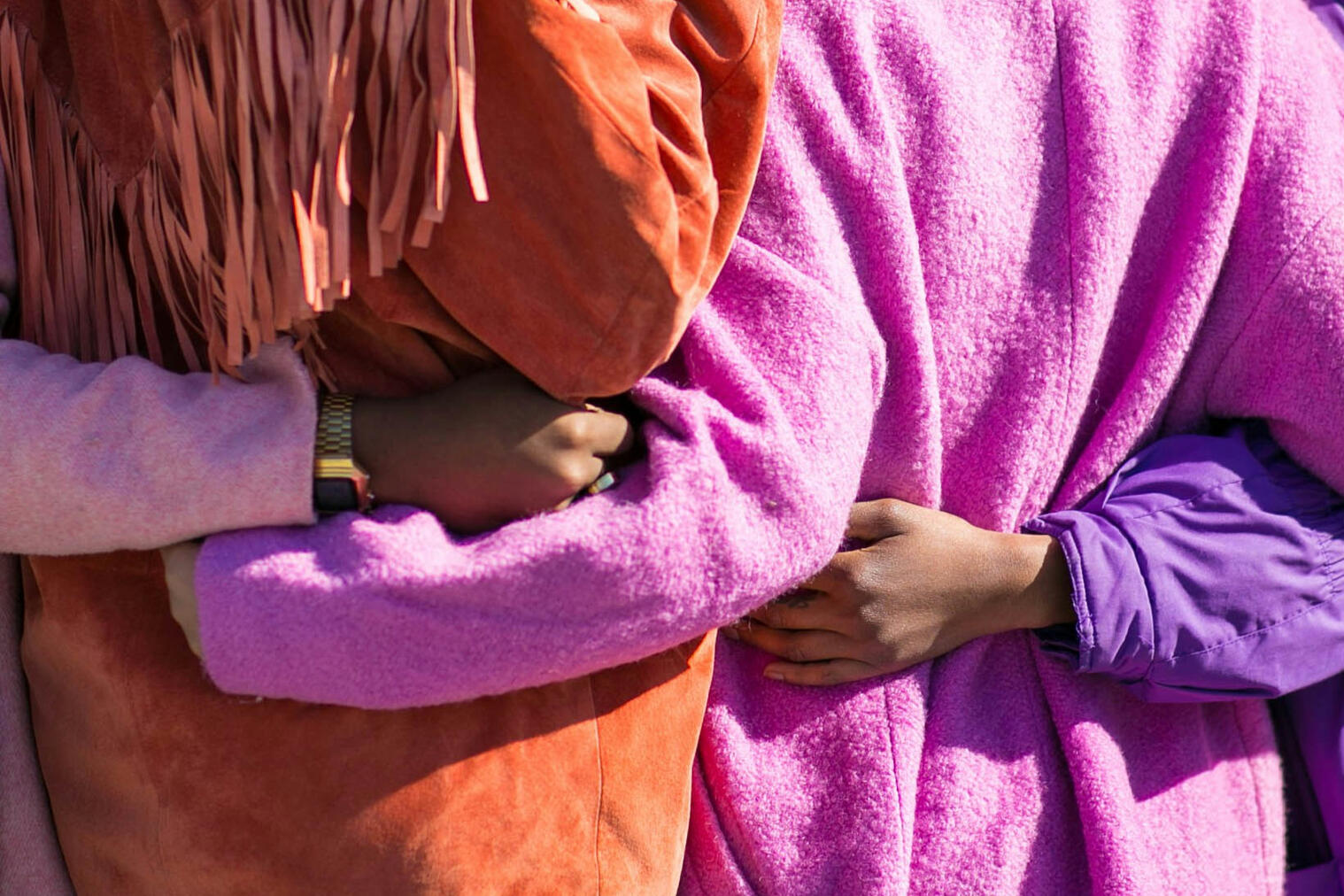 Untitled Four women holding each other's sides wearing bright pinks and oranges.