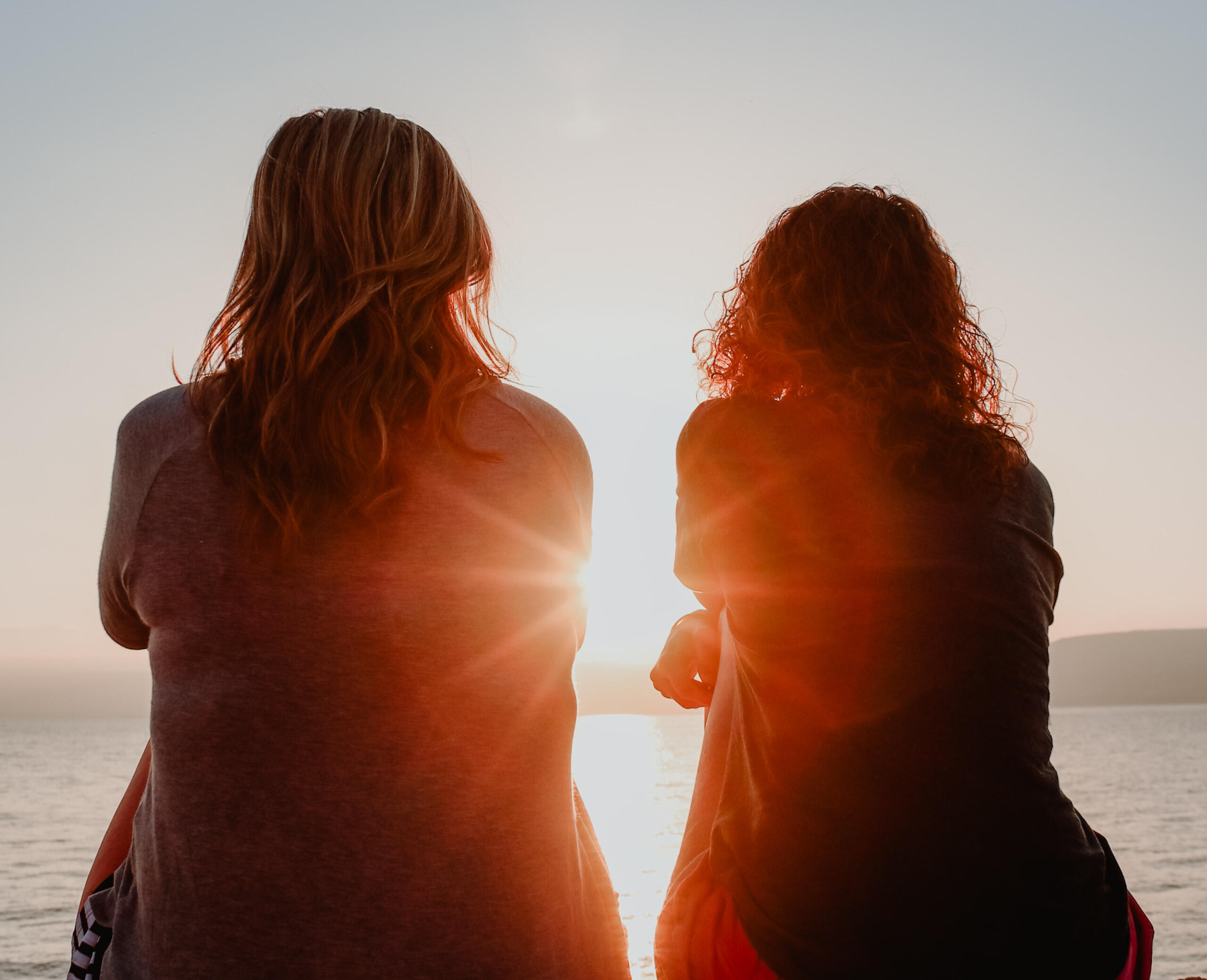Two women sitting with their backs to the camera, watching the sunset.